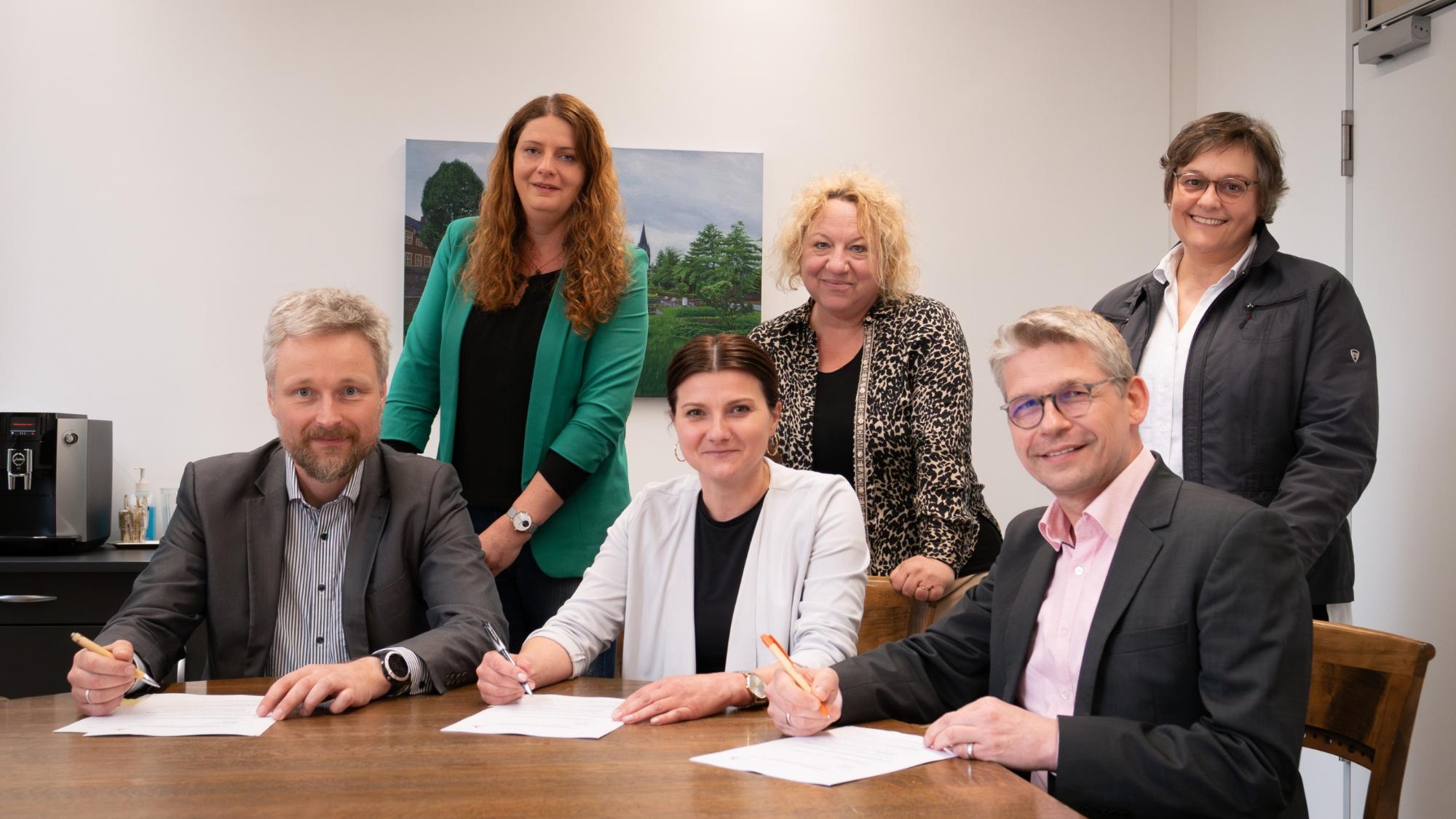 Bei der Vertragsunterzeichnung (sitzend v.l.) Timo Plaß (Sozialdienst katholischer Frauen für die Dekanate Ahaus und Vreden), Marina Bänke (Stadt Ahaus) und Peter Schwack (Caritas-Vorstand) gemeinsam mit (v.l.) Claudia Mersmann, Silke Herbrand und Vera Reimer.