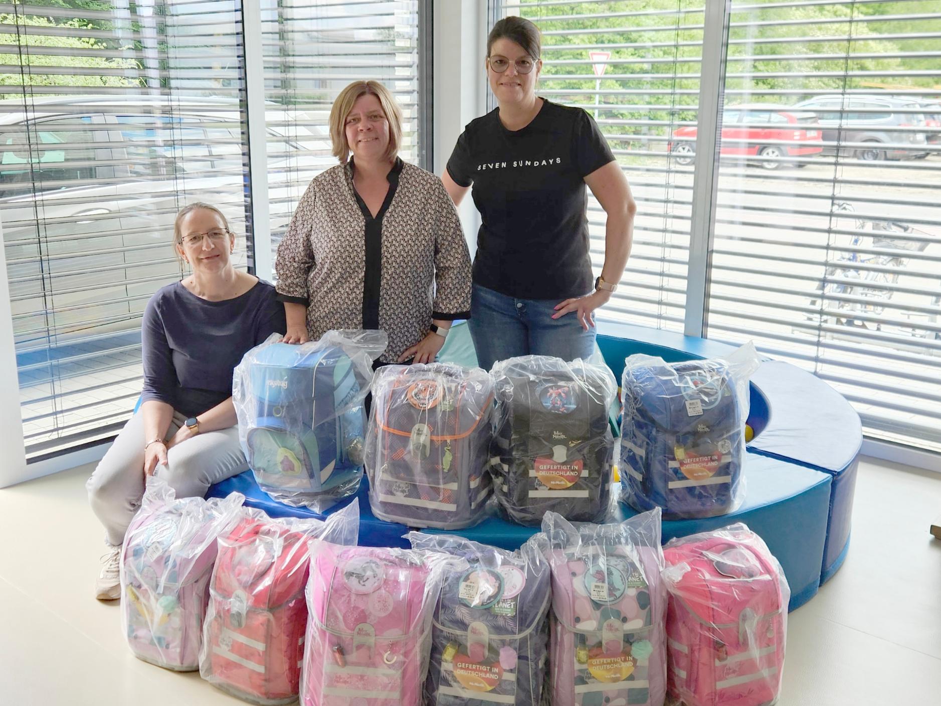 Daniela Brillert, Ramona Rensing und Marlene Terbeck stehen hinter 10 gespendeten Schultornistern.