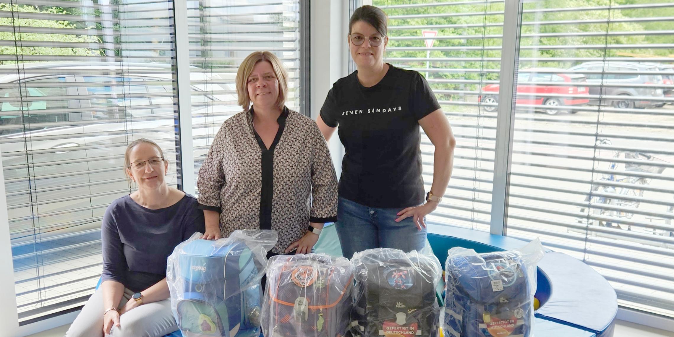 Daniela Brillert, Ramona Rensing und Marlene Terbeck stehen hinter 10 gespendeten Schultornistern.
