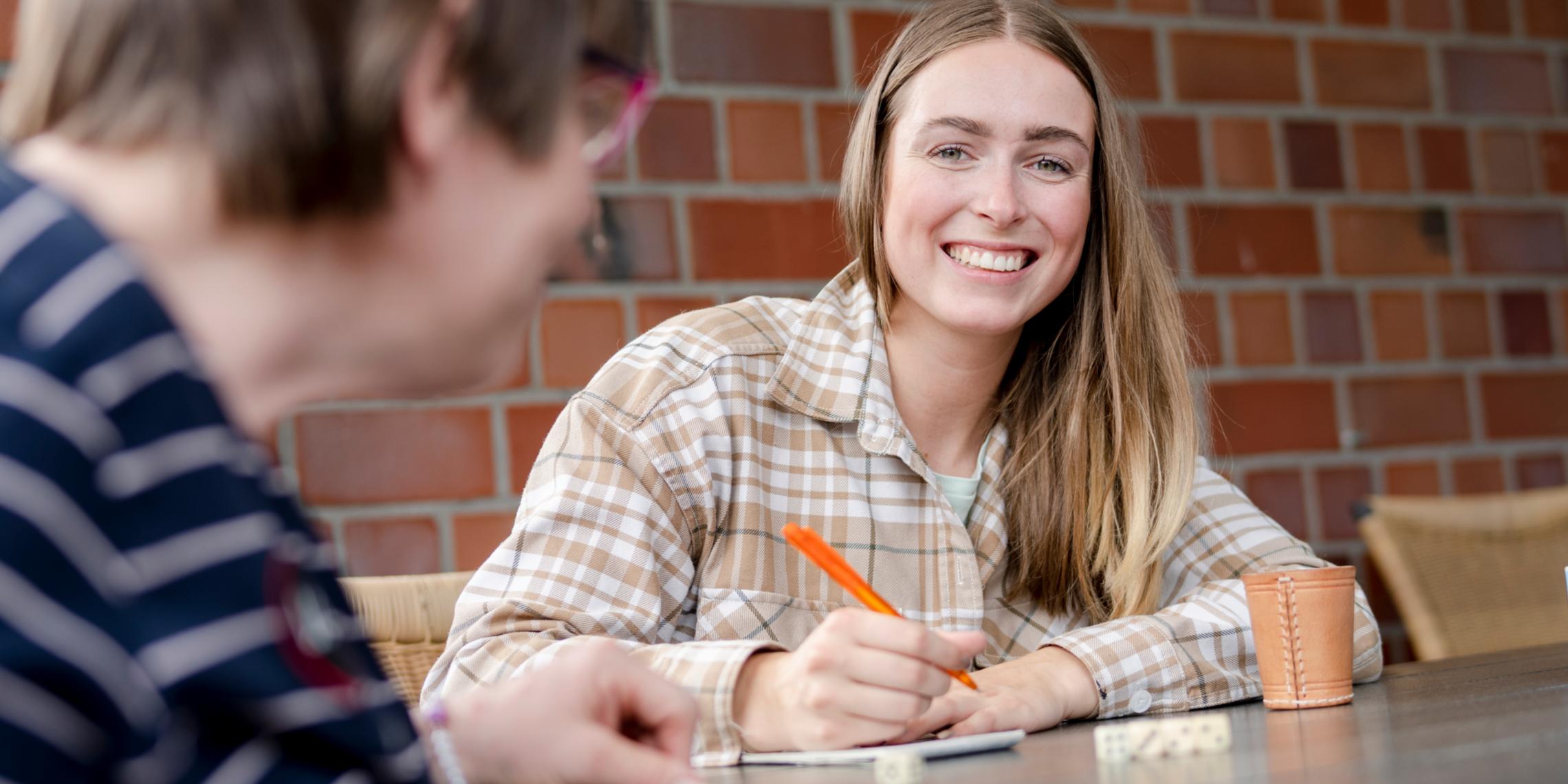 Lernt unsere Ausbildungsberufe bei der Nacht der Ausbildung kennen! Auszubildende sitzt lächelnd am Tisch und schreibt etwas auf