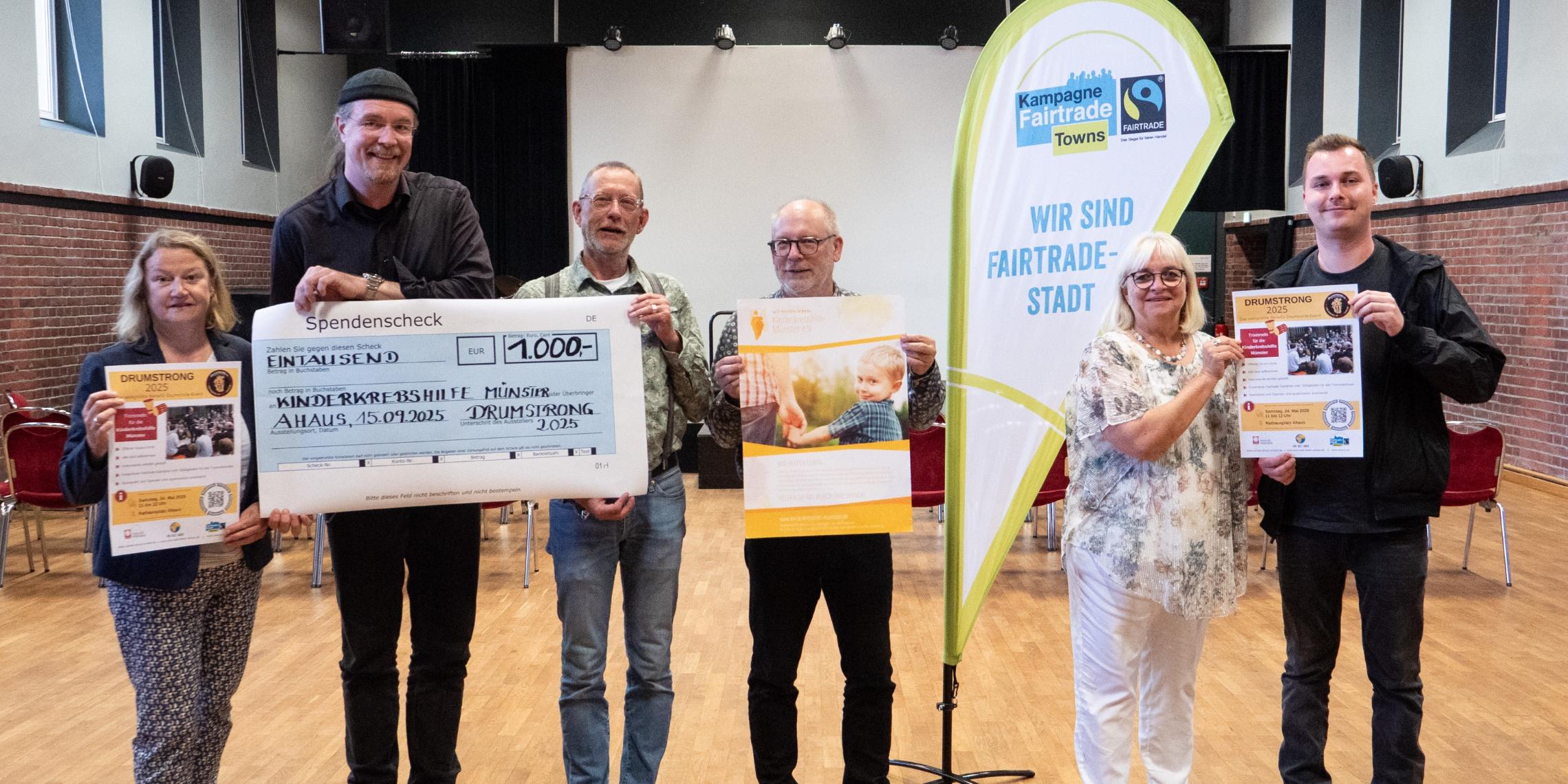 Sechs Personen halten Plakate und einen symbolischen Scheck in die Kamera. Auf dem Scheck ist eine Spendensumme von 1000 Euro eingetragen.