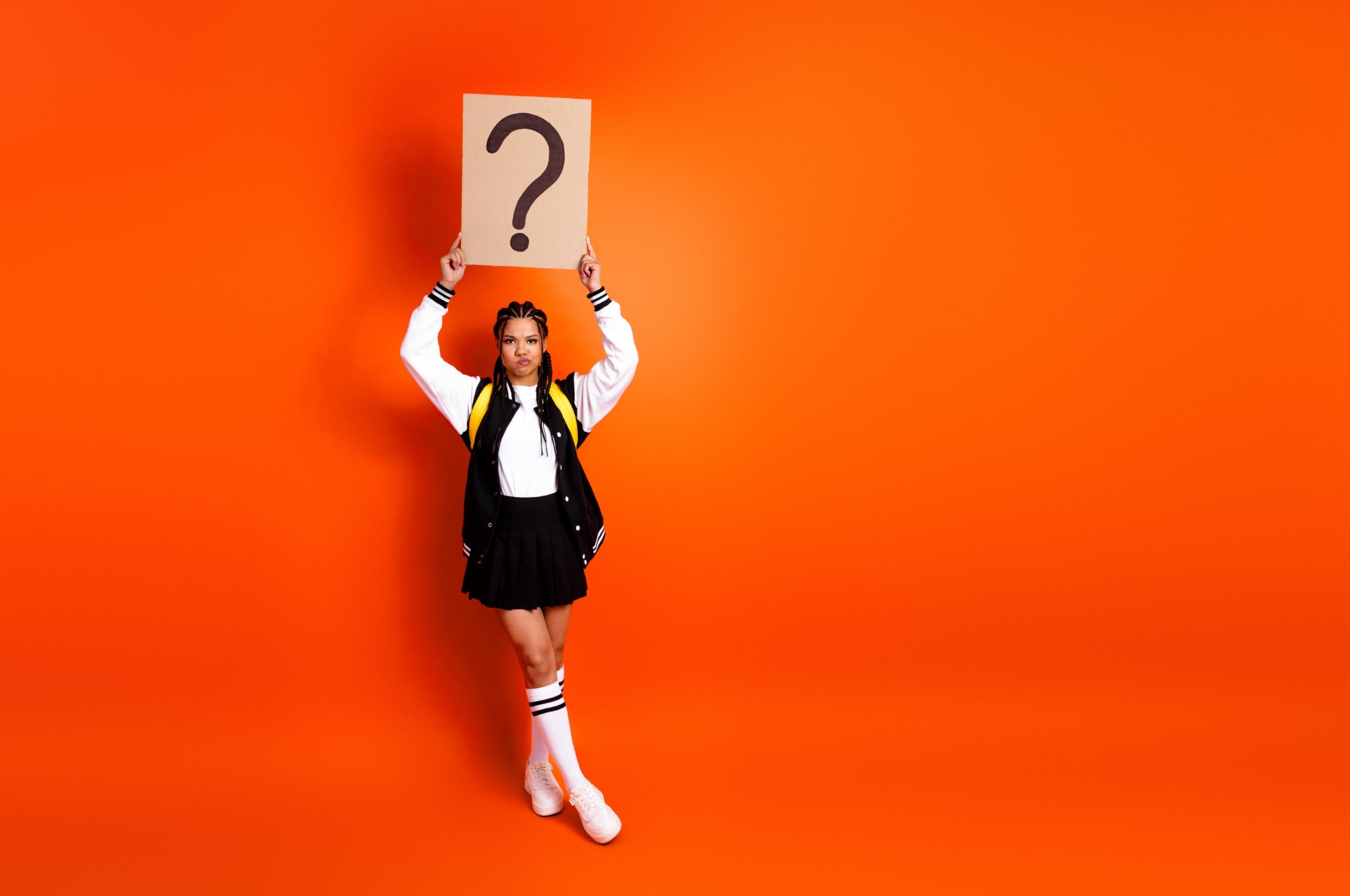 Eine junge Frau hält mit beiden Händen ein Plakat hoch, auf dem ein Fragezeichen steht.