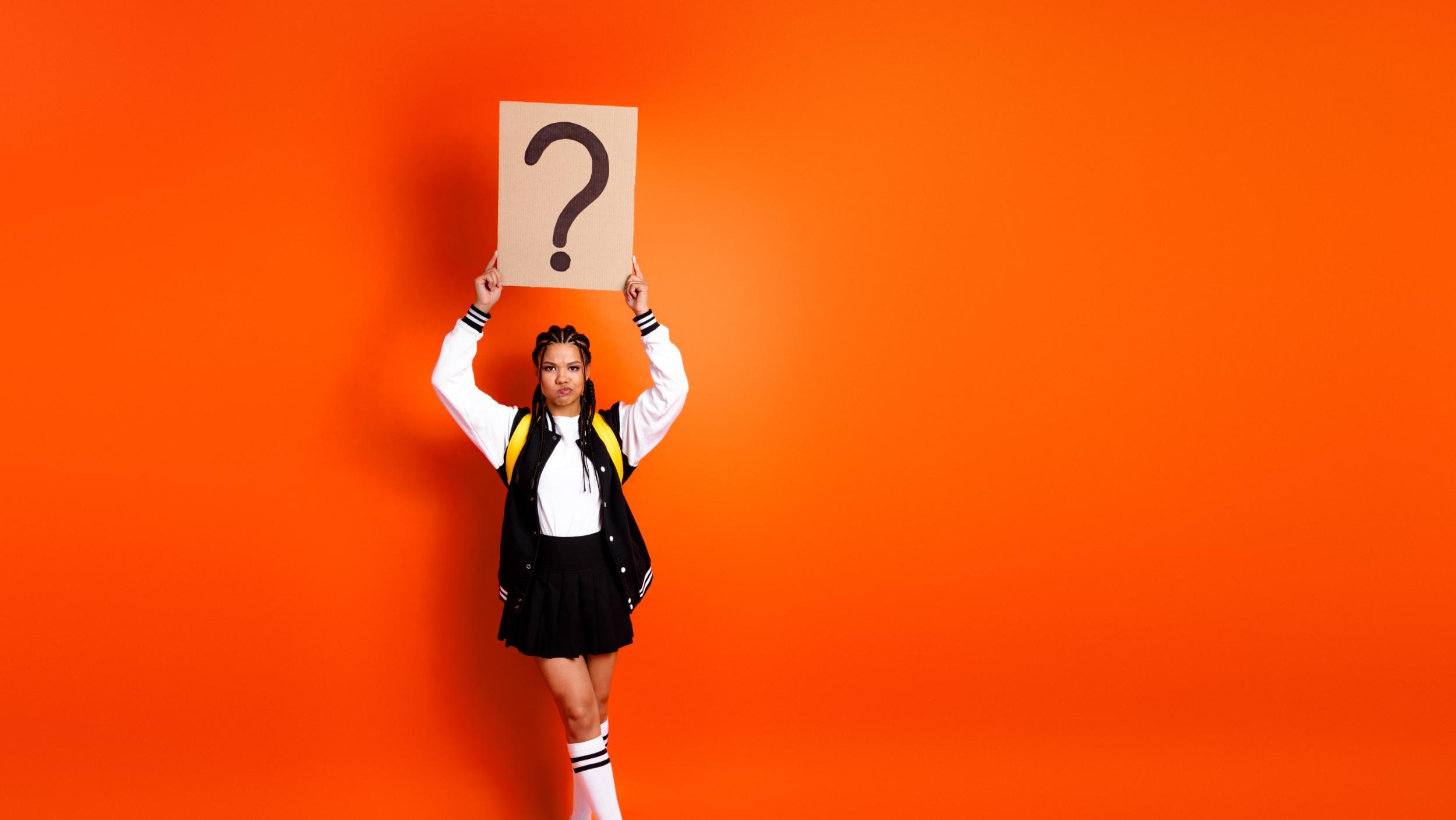 Eine junge Frau hält mit beiden Händen ein Plakat hoch, auf dem ein Fragezeichen steht.